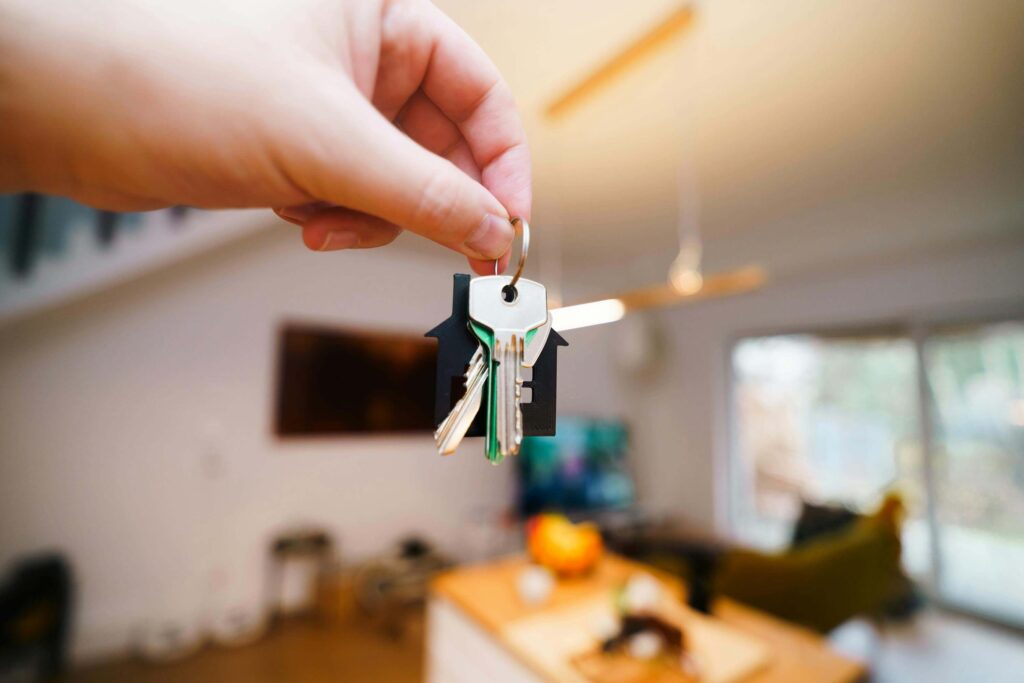 Mão segurando chave de casa com fundo embaçado de imóvel novo