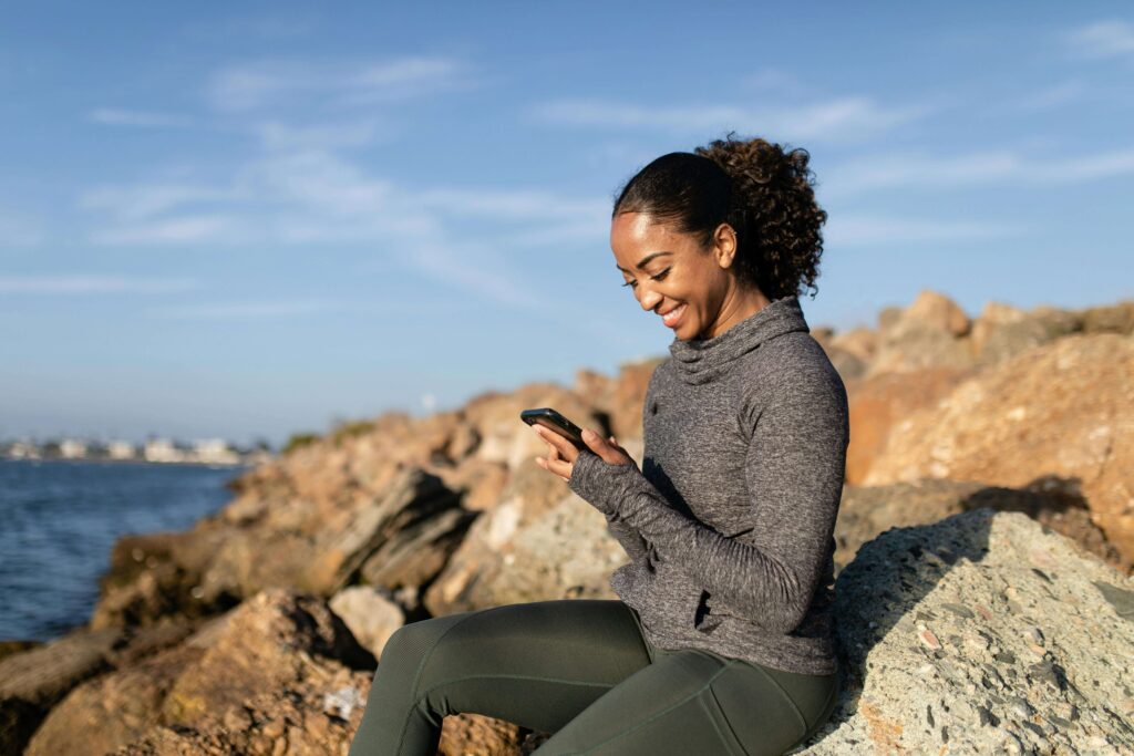 Jovem sorridente olhando um aplicativo financeiro no celular, transmitindo sensação de controle e bem-estar com as finanças.
