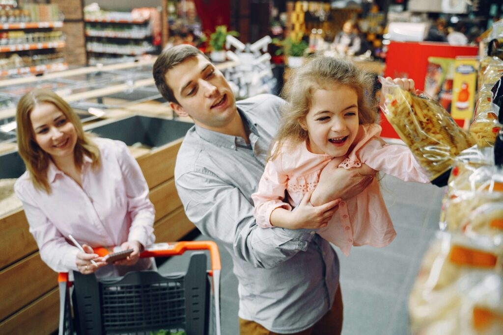 Criança escolhendo produtos no mercado com a supervisão de um adulto, aprendendo a lidar com dinheiro.