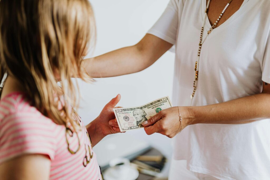 Pai e mãe explicando para os filhos o valor do dinheiro usando notas e moedas reais.