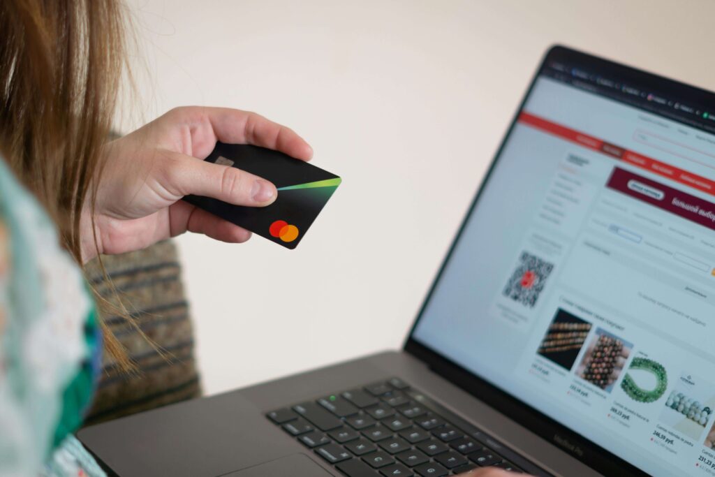 Pessoa segurando cartao e com computador na frente em um site de compras, comprando alguma coisa impulsivamente.