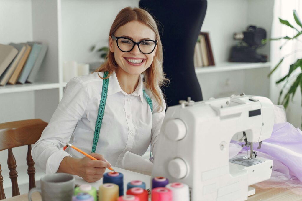Mulher com uma fita de medir no pescoço sorrindo e costurando fazendo um trabalho manual, simbolizando o DIY e a renda extra para decorar.