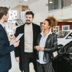 Casal conversando com vendedor de carro, simbolizando a decisão financeira sobre mobilidade em 2025.