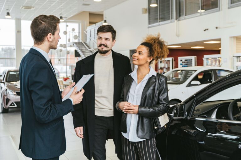 Casal conversando com vendedor de carro, simbolizando a decisão financeira sobre mobilidade em 2025.